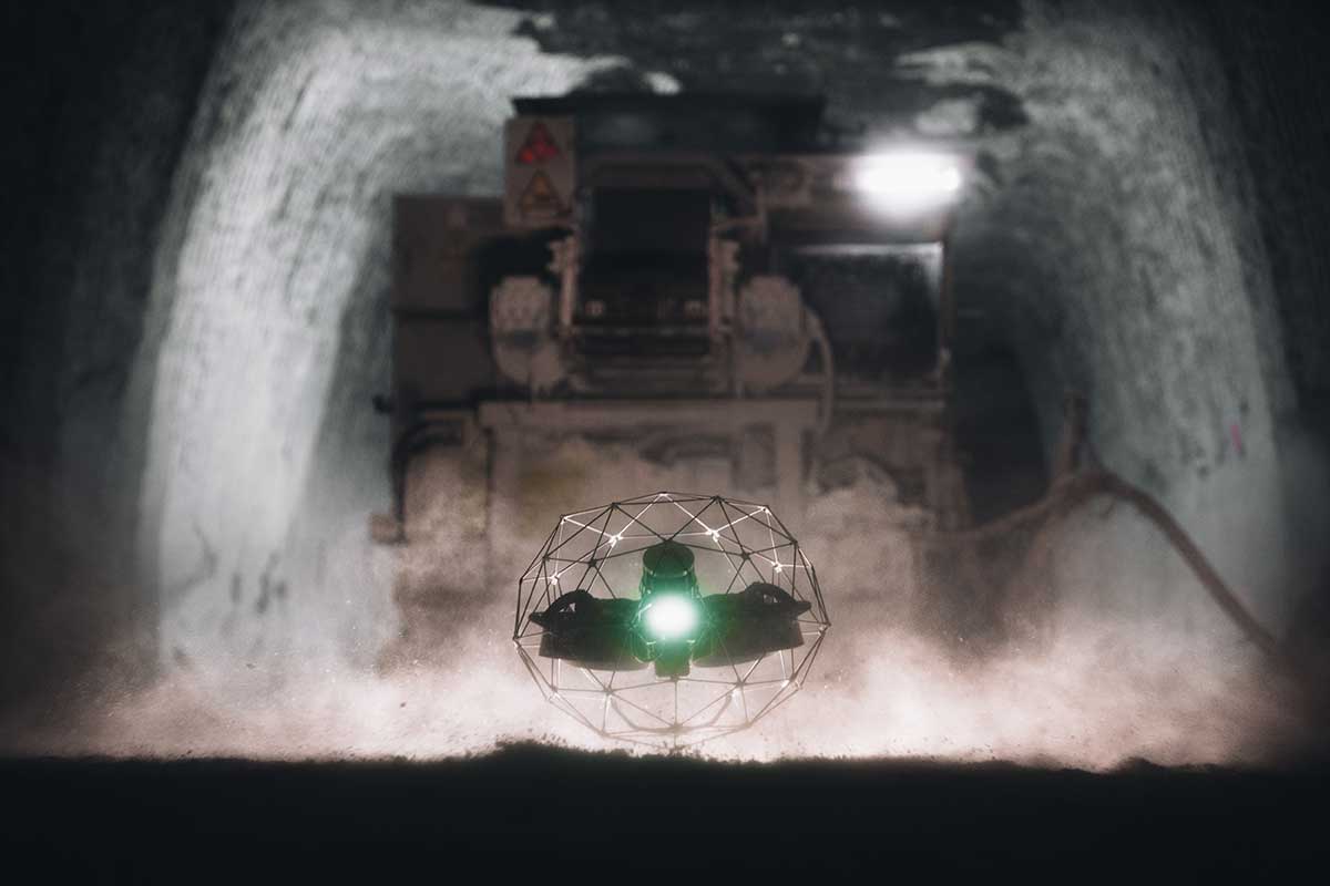 Flyability Elios drone in its protective cage hovering inside a dusty mine tunnel