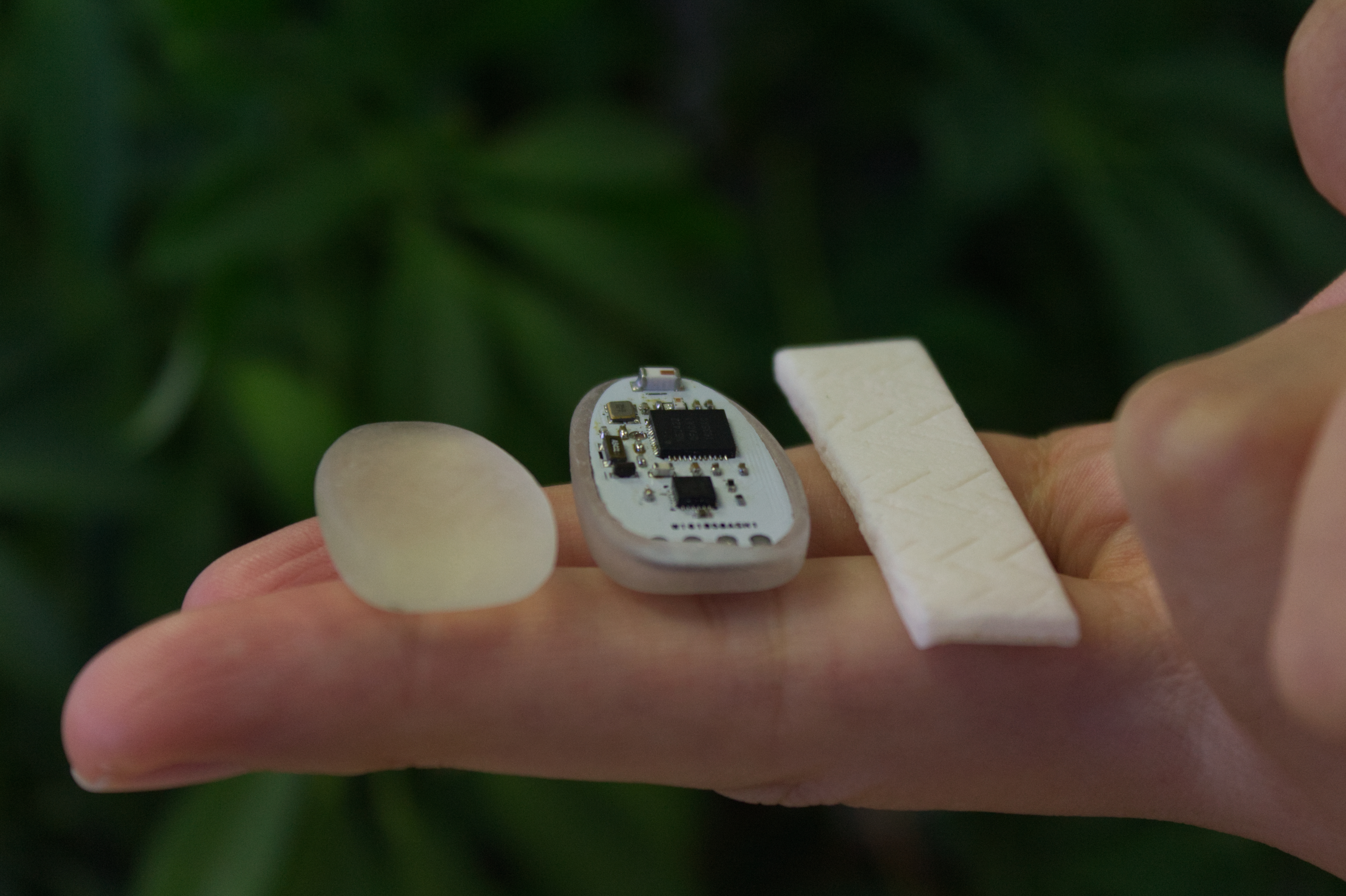 ChewIt device components — silicone shell, PCB module and fabric strap — held on a fingertip